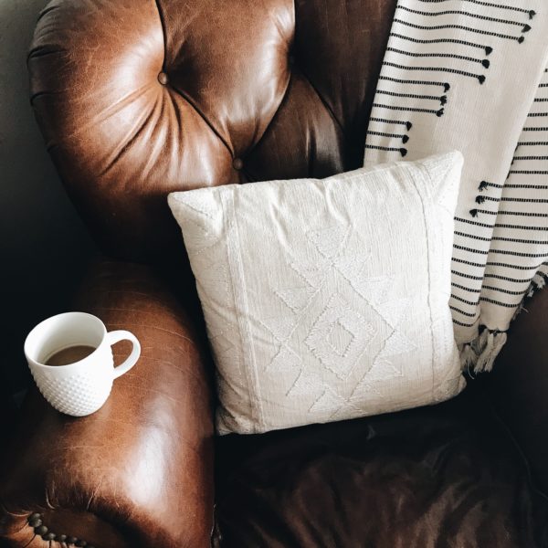 brown leather chair with white pillow and blanket on it and a mug of tea on the armrest